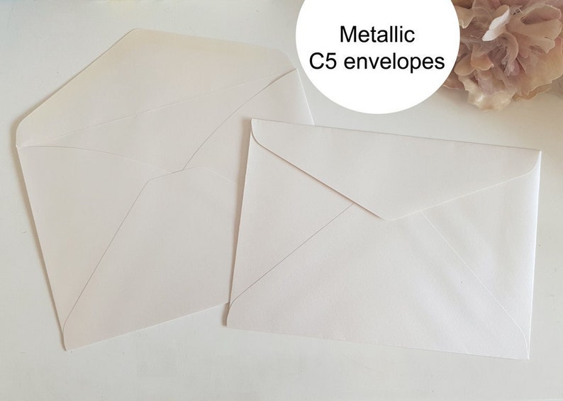 May include: Two white C5 envelopes with a metallic finish. The envelopes are lying flat on a white surface.