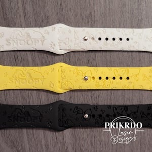 Puede incluir: Tres correas de reloj en blanco, amarillo y negro. Cada correa presenta un diseño de Snoopy y la palabra "SNOOPY". Las correas tienen múltiples agujeros para ajustar y un cierre plateado. Las correas están hechas de un material flexible.