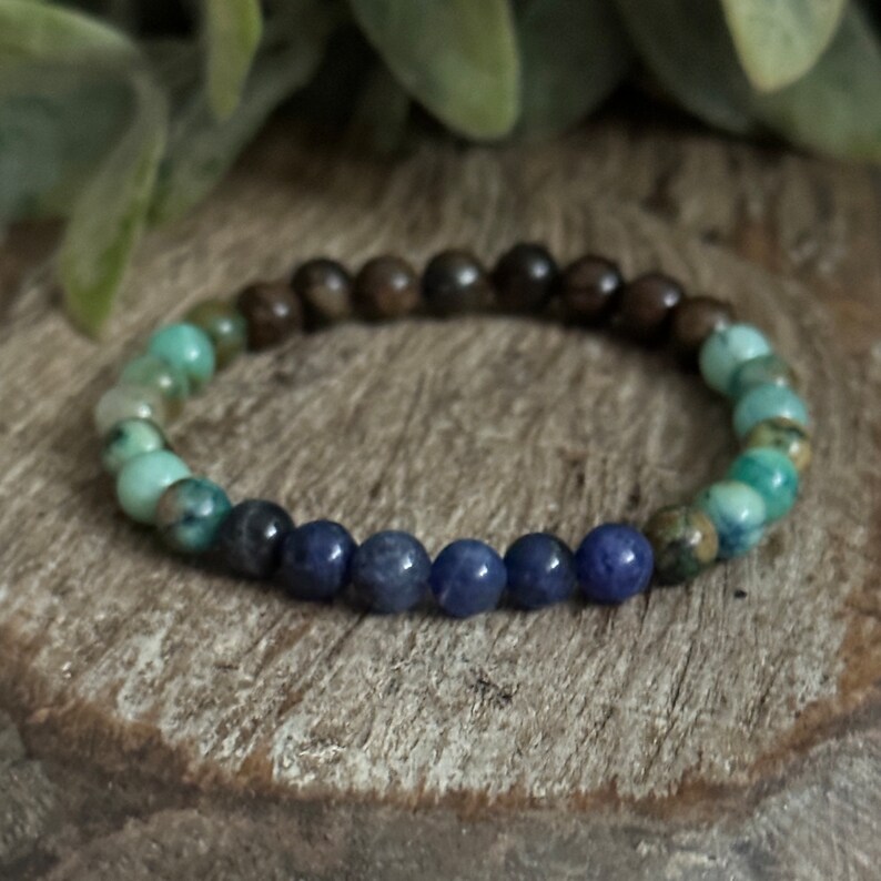 May include: A beaded bracelet with brown, green, and blue beads. The beads are arranged in a gradient pattern, starting with brown, then green, and finally blue.