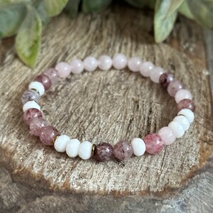 Op de afbeelding: Een roze en witte kralen armband met gouden accenten. De armband is gemaakt van kleine, ronde kralen en is geregen op een elastisch koord.