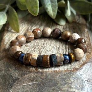 May include: A brown and beige gemstone bracelet with blue and gold accents. The bracelet is made of round beads and is strung on a stretchy cord.
