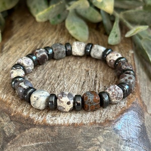 May include: A bracelet made of brown, gray, and black stones. The bracelet is made of round beads and has a metal clasp.