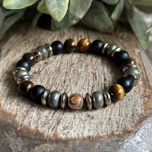 May include: A beaded bracelet with black, brown, gold, and silver beads. The bracelet has a unique, eye-catching design.