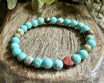 Puede incluir: Un brazalete de cuentas turquesa y marrón con un dije de corazón rojo.