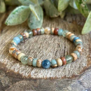 Puede incluir: Un brazalete de cuentas con una mezcla de piedras marrones, beige, azules y verdes. El brazalete está hecho con piedras naturales y es un gran accesorio para cualquier ocasión.
