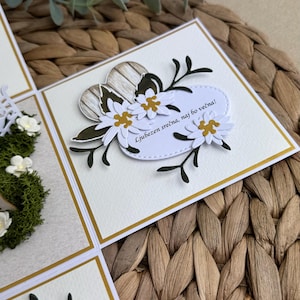 Op de afbeelding: Een witte kaart met een gouden rand en een bloemmotief. De kaart heeft een wit hart met een houtnerfpatroon en de tekst "Ljubezen srečna, naj bo večna!" wat vertaalt naar "Gelukkig liefde, mag het eeuwig zijn!"