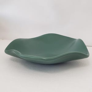 May include: A dark green, ceramic, wavy-edged bowl. The bowl has a smooth, glossy finish and a shallow, open design. The bowl is set against a white background.