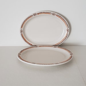 May include: Two white oval plates with a brown and gold leaf design around the rim.