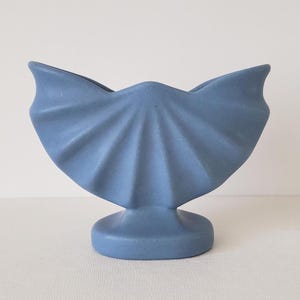 May include: A blue ceramic vase shaped like a seashell with a wide, open top and a round base.