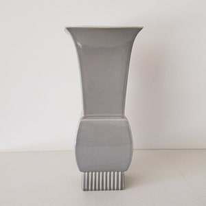 May include: A gray ceramic vase with a square base and a flared top. The vase has a smooth, glossy finish.