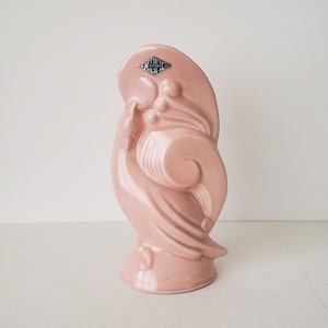 May include: A pink ceramic vase with a stylized design, featuring a swirl pattern and a raised diamond-shaped label that reads "Hall's Pottery".