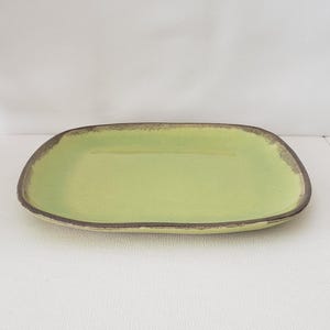 May include: A rectangular ceramic serving platter with rounded corners. The platter has a light green interior and a dark brown rim. The background is a plain white surface.