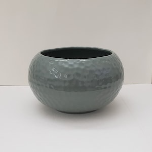 May include: A round, hammered, light green ceramic planter. The planter has a smooth, glossy finish.