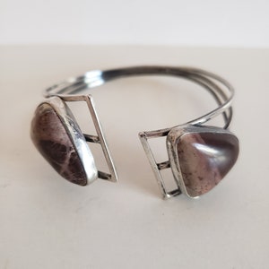 May include: A silver bangle bracelet with two triangular shaped brown and white stones. The bracelet is open and has a simple design.