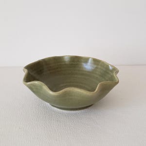 May include: A small, green ceramic bowl with a wavy rim. The bowl has a subtle, textured surface.