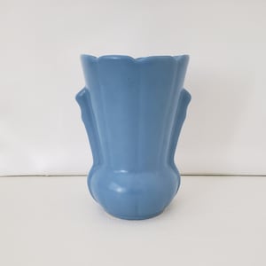 May include: A light blue ceramic vase with a fluted design and two handles. The vase has a rounded bottom and a flared top.