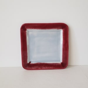 May include: A square ceramic dish with a white interior and a dark red rim.