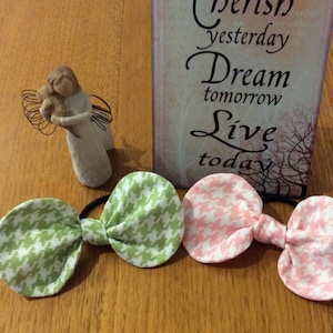 Peut inclure: Trois chouchous en tissu à motif pied-de-poule vert et rose, à côté d'une pancarte décorative avec l'inscription "Cherish yesterday Dream tomorrow Live today". Une petite figurine d'ange est également présente.