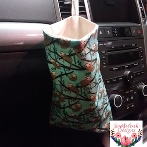 Op de afbeelding: Een turquoise en bruine autovuilnisbak met een sloths-patroon en een witte voering. De vuilnisbak hangt aan de hoofdsteun van een auto. De tekst "SewSarah Designs" is zichtbaar in de rechterbenedenhoek van de afbeelding.