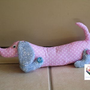 May include: A pink and blue fabric dachshund doorstop with white polka dots. The doorstop has a blue button on the side and a pink button on the tail.