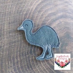 May include: A gray felt applique of an emu, a flightless bird native to Australia. The emu is standing with its legs outstretched and has a simple, smiling face.
