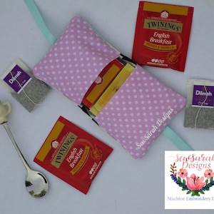 Puede incluir: Una bolsa de tela rosa con lunares blancos y cierre de cremallera. La bolsa está llena de bolsitas de té, incluyendo bolsitas de té Twinings English Breakfast Honey & Vanilla y Dilmah. La bolsa está etiquetada con "Sew Sarah Designs".