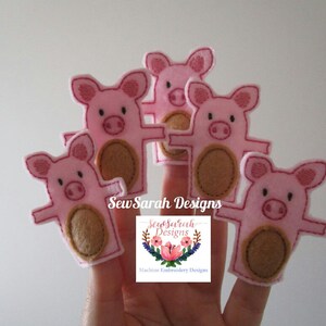 May include: Five pink pig finger puppets with brown felt noses and brown felt finger holes. The puppets are on a hand, and the text "Sew Sarah Designs" is visible below the puppets.