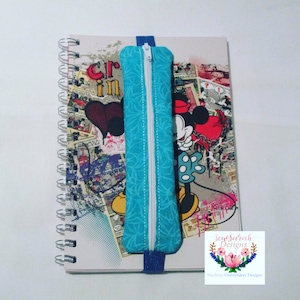 Peut inclure: Une trousse à crayons zippée turquoise avec un motif floral blanc et une fermeture éclair blanche. La trousse est attachée à un carnet avec un élastique bleu. La couverture du carnet présente une image de dessin animé de Mickey Mouse et un cœur rouge.