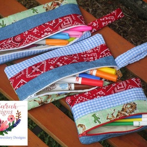 May include: Three zippered pouches made of denim, red and white gingham, and green fabric with a western theme. The pouches are filled with colorful markers and are sitting on a wooden surface. SewSarah Designs Machine Embroidery Designs.
