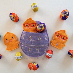 May include: Purple felt Easter egg basket with two felt chicks, one with glasses and a tie, and the other with glasses. The basket is filled with Cadbury Creme Eggs and other chocolate eggs.