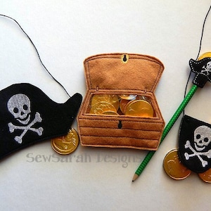 May include: A set of felt pirate-themed accessories for kids, including a black felt pirate hat with a skull and crossbones, a brown felt treasure chest with gold coins, and a green felt pirate sword with a black felt skull and crossbones.