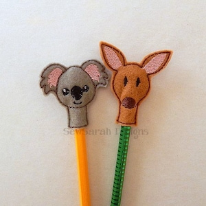 May include: Two pencil toppers: a grey koala with pink ears and a brown kangaroo with pink ears. The koala is on an orange pencil, and the kangaroo is on a green pencil. The text "SewSarah Designs" is visible.