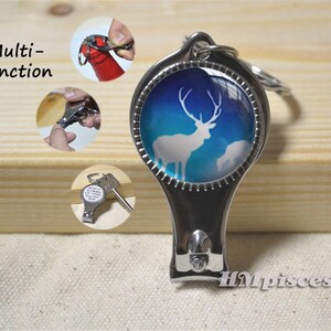 May include: A multi-function nail clipper with a deer silhouette design. The clipper has a silver finish and a blue and white background. The image also shows the clipper being used as a bottle opener and a key.