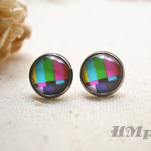 May include: A pair of silver stud earrings featuring a colourful static television screen design. The earrings are round and have a black border.