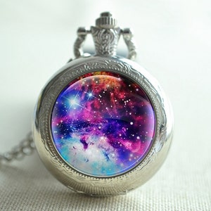 May include: A silver pocket watch necklace with a round glass face featuring a colorful galaxy image. The galaxy is a mix of pink, purple, blue, and white with stars.