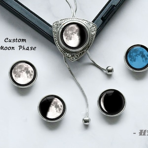 May include: A silver necklace with a moon phase pendant and five interchangeable moon phase charms. The charms are silver with a clear glass top and a moon phase image inside. The moon phases include a full moon, a crescent moon, a half moon, a new moon, and a blue moon.