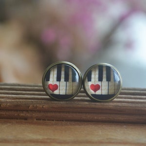 May include: A pair of round, bronze-colored earrings with a white and black piano key design and a red heart on each earring.