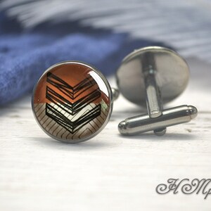 May include: A pair of cufflinks with a black and white geometric design on a brown background. The cufflinks are silver.