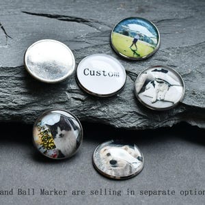 May include: Five different golf ball markers with various images. The markers are round and silver with a clear glass top. The images include a golfer, a dog, a cat, a custom text, and a blank marker.