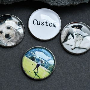 May include: Four round golf ball markers with different images. One marker has a white background with the word "Custom" printed in black. Another marker has a photo of a dog. Another marker has a photo of a dog. The last marker has a photo of a person playing golf.