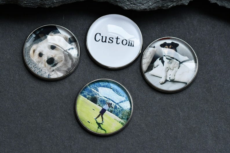May include: Four round golf ball markers with different images. One marker has a white background with the word "Custom" printed in black. Another marker has a photo of a dog. Another marker has a photo of a dog. The last marker has a photo of a person playing golf.