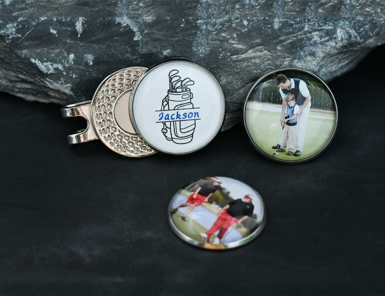 May include: Three golf ball markers. One features a black and white illustration of a golf bag with the name "Jackson" printed on it. The other two markers feature photos of people playing golf.