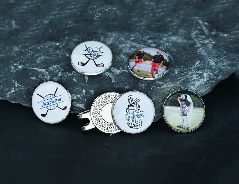 May include: Set of six personalized golf ball markers with different designs.  The markers feature names, golf clubs, golf balls, and photos.  The markers are white with blue and black accents.