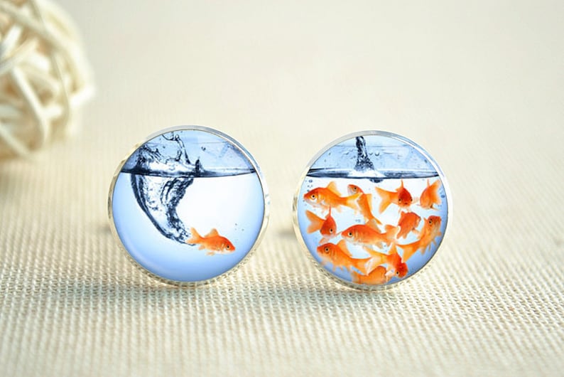 May include: A pair of cufflinks with a design of goldfish swimming in a bowl. One cufflink shows a single goldfish jumping out of the water, while the other cufflink shows a group of goldfish swimming together.
