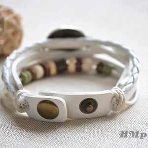 May include: White leather bracelet with a braided design and brown and white beads. The bracelet has a metal clasp.