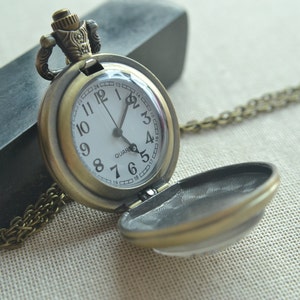 May include: A bronze pocket watch with a white face and black hands. The watch has a chain attached to it and is open to reveal a blank interior.