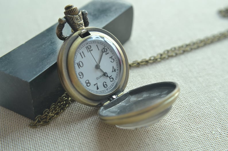 May include: A bronze pocket watch with a white face and black hands. The watch has a chain attached to it and is open to reveal a blank interior.