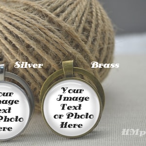 May include: Two pendant necklaces, one silver and one brass, each with a circular glass cabochon. The cabochons display the text "Your Image Text or Photo Here". A ball of twine is in the background.