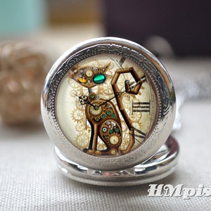 K&ouml;nnte beinhalten: Ein silberfarbener Taschenuhr-Anh&auml;nger mit einer Katzenillustration, die aus Zahnr&auml;dern und Uhrwerksteilen besteht. Die Katze hat ein gelbes und ein gr&uuml;nes Auge. Der Text HMpisces ist in der unteren rechten Ecke des Bildes aufgedruckt.