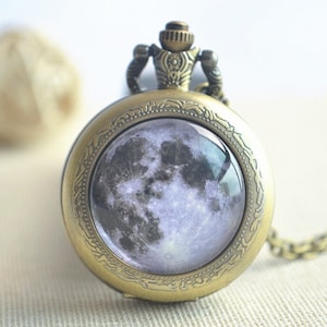 Puede incluir: Un reloj de bolsillo de bronce con una cadena, que presenta una imagen de luna llena en la esfera.
